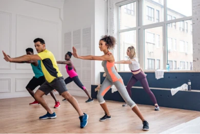 Na foto, há quatro pessoas que estão em um estúdio de dança realizando simultaneamente um dos passos da modalidade. #ParaTodosVerem