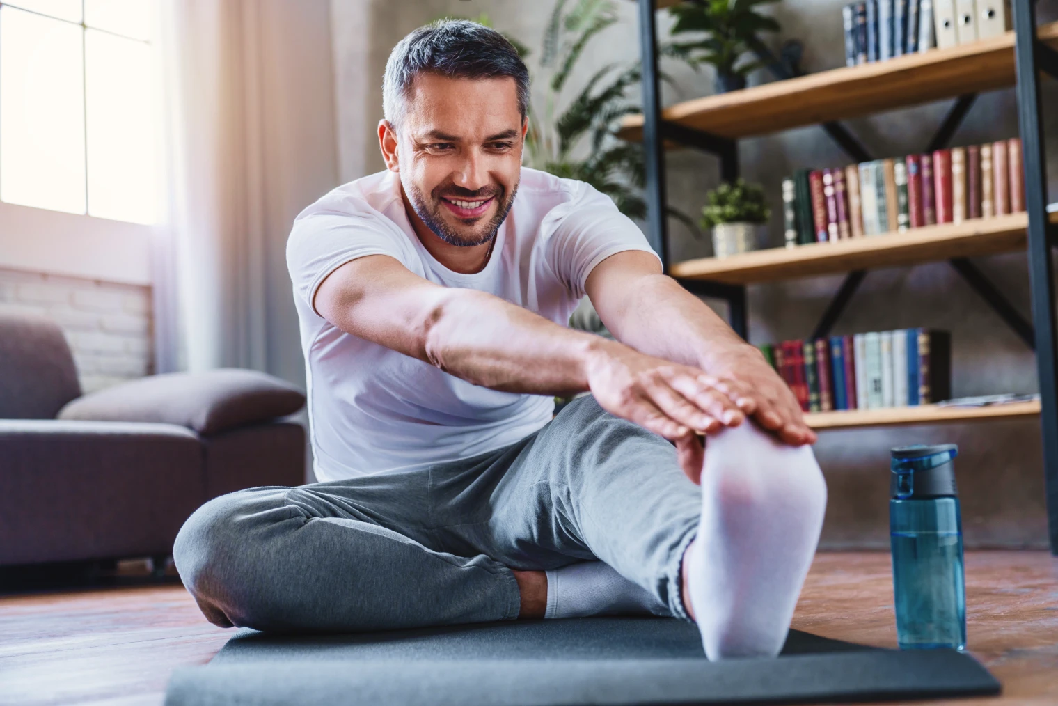 A imagem tem um homem se alongando em casa.