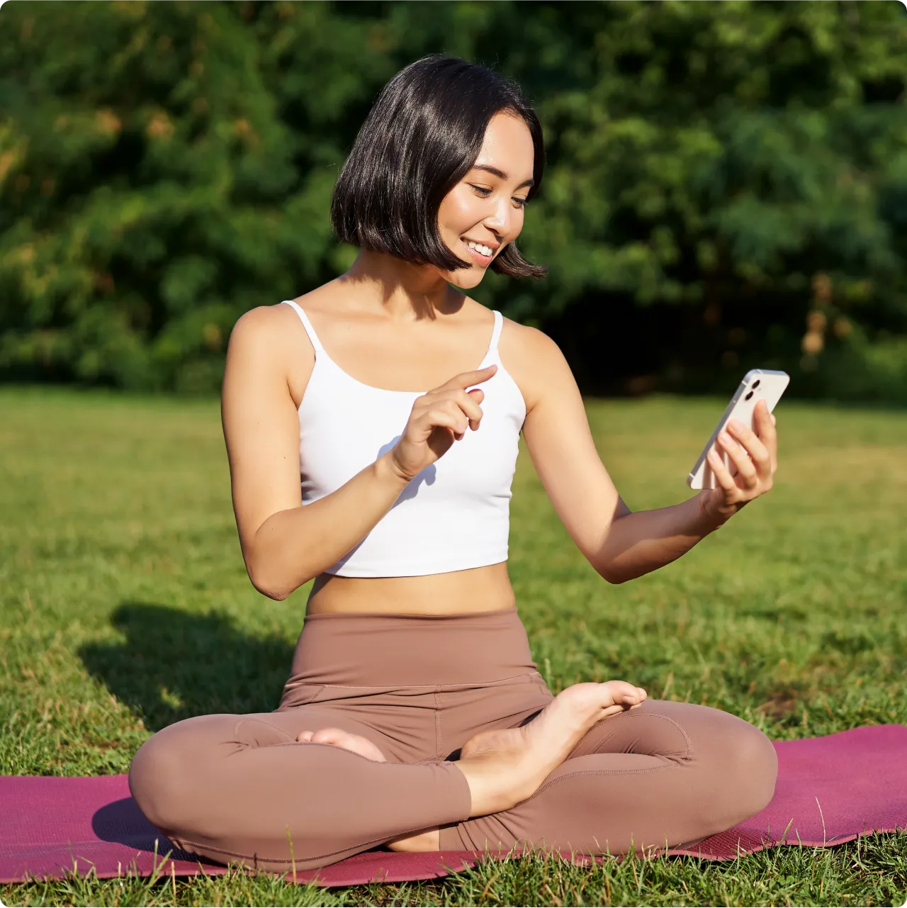 Uma mulher em um campo verde praticando yoga e olhando para o celular sorrindo