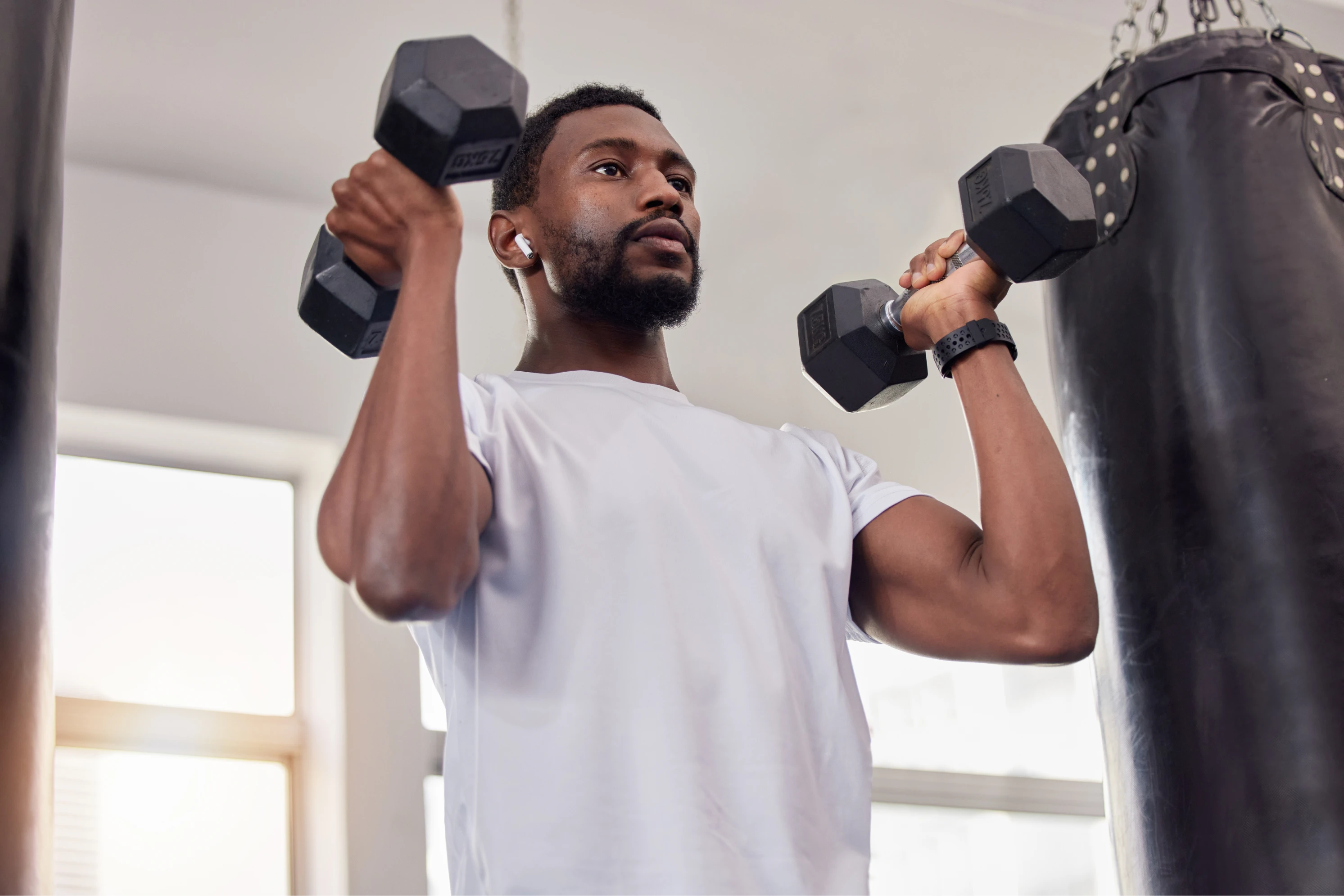 A imagem tem um homem fazendo exercício. Ele está segurando um par de halteres. 